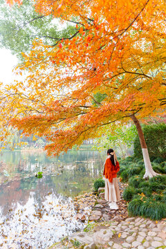 Serene autumn escape, A young woman standing under vibrant autumn foliage by a peaceful pond