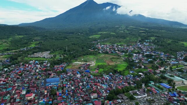 Slow drone footage flying above Lucban Bypass Road, Lucban, Quezon, Philippines featuring rural neighborhoods, lush rice paddies, scenic countryside roads, and Mount Banahaw de Lucban during daytime.
