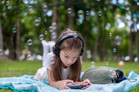 Young mixed race girl lying on a blanket and using a smartphone surrounded by bubbles in the park.