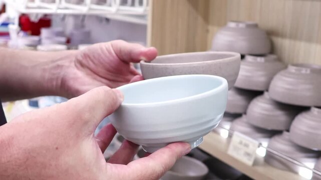 Man compares two ceramic bowls by size, shape and design before purchase. Concept of home shopping, kitchenware selection, consumer choice and household products.