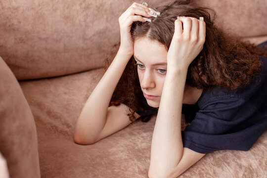 Young woman lying on sofa holding head with hands looking sad and stressed. Anxiety, depression and mental health problem concept. Teenage loneliness and emotional burnout at home