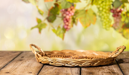 Fototapeta premium Flat wicker tray on wooden table with blurred grapes and vine leaves for rustic autumn product background