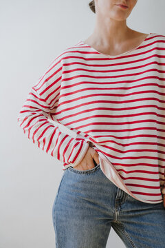 Casual Female Outfit Featuring Red Striped Sweater And Blue Jeans Against Plain White Wall