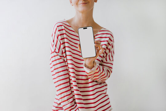 Woman In Red And White Striped Long Sleeve Shirt Presenting Smartphone Screen Mockup Standing Against Plain Wall