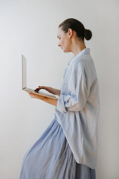 Standing Profile View Of Woman Working On Laptop Computer Next To Neutral Wall