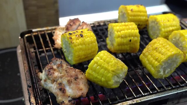 Grilling corn. A man flips hot corn with tongs.