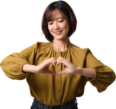 Happy asian woman making heart hand gesture while smiling wearing stylish yellow blouse against clean plain background for copy space