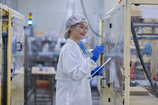 Female worker focused on factory industry inspection wearing uniform holding clipboard ensuring safety production line quality control manufacturing plant checking process looking confident