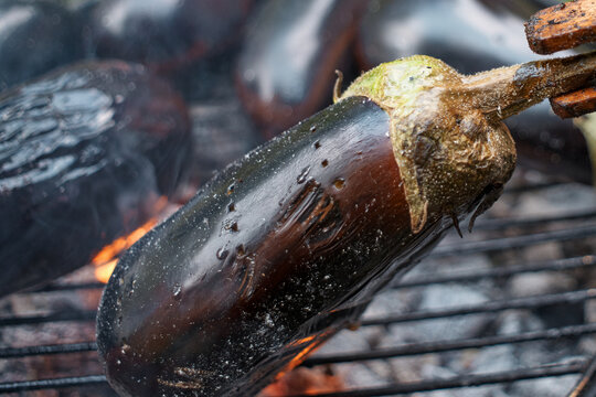 Close-up of a fresh purple eggplant being grilled on a hot charcoal barbecue pit