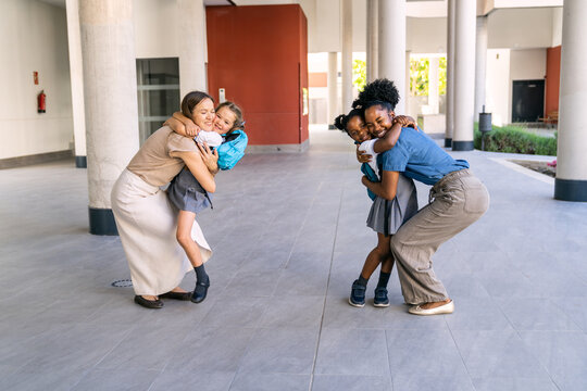 Multiethnic mothers embracing their elementary school daughters at the school entrance on the first day, celebrating education and family