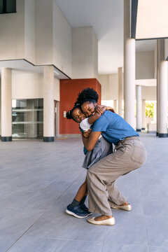 Happy african american mother embracing her young schoolgirl daughter in uniform, celebrating the first day back to school
