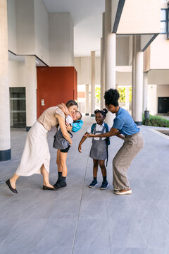 Multiethnic mothers greeting their daughters, one hugging a girl, the other high fiving, on the first day of school