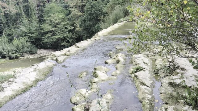 Prospettiva della Cascata del Sasso, con l'acqua che scivola tra i massi circondata da una fitta foresta ripariale