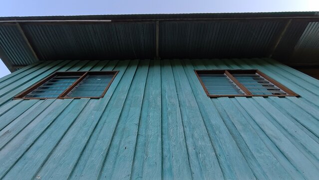 Worm eye view of a blue painted wooden building exterior with two glass louver windows and corrugated roof