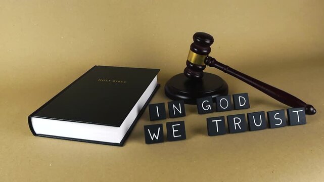 Still life arrangement with the Holy Bible, a judge's gavel, and the motto 'In God We Trust' on a brown background, symbolizing the foundation of justice on religious and moral principles