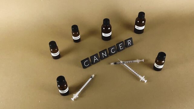 Conceptual representation of cancer treatment and research, featuring the word cancer surrounded by vaccine vials and syringes on a neutral background, symbolizing medical advancement and hope