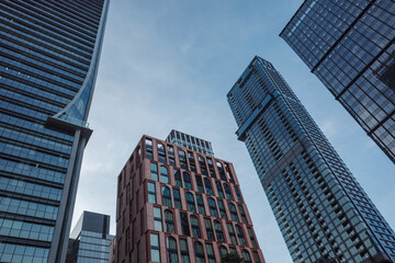 Fototapeta premium Low-angle view of multiple modern corporate skyscrapers featuring glass and brick architectural facades under a clear blue sky during the day.
