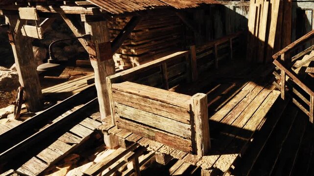 The scene shows a rustic wooden structure beside train tracks. It is surrounded by rocks and has an old lamp hanging. Sunlight creates shadows on the ground.