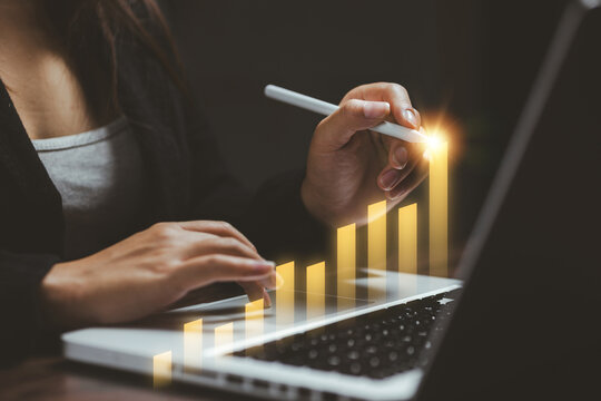 Businesswoman analyzes a glowing growth bar chart on laptop with digital pen, representing financial performance, business analytics, investment, strategy, profit, growth, and success.
