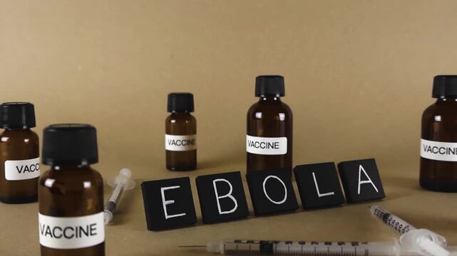 Medical vials labeled vaccine and syringes surrounding the word Ebola, representing the global effort to develop a treatment and immunization for the deadly hemorrhagic fever virus