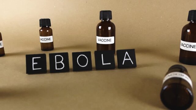 Small brown glass bottles with vaccine labels surrounding the word Ebola, representing the scientific research for a cure, prevention efforts, and the fight against the deadly viral disease