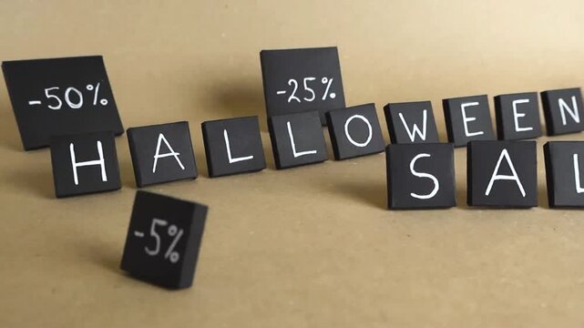 Black paper squares with handwritten Halloween sale text and various discount percentages moving across a light brown, recycled paper background, representing a special seasonal promotion