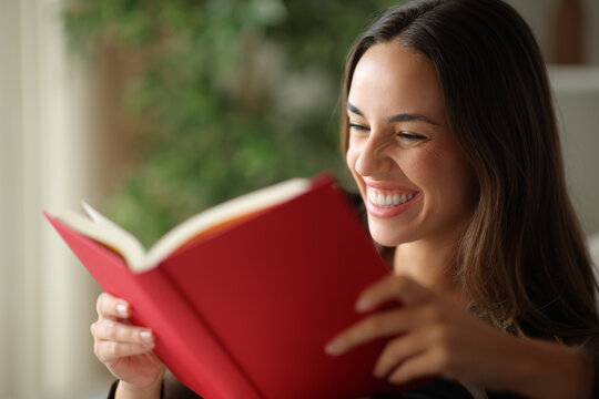 Happy woman reading a red paper book in a house indoor