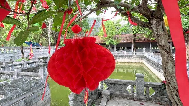 Red paper lantern hanging on a tree at a traditional Vietnamese temple in Hanoi. Symbolizes cultural heritage and festive celebrations. Ideal for travel and tourism content