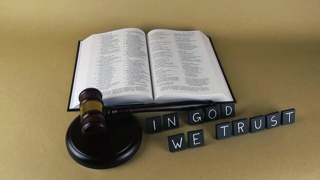 Religious and legal symbols combining as an open Holy Bible sits next to a judge's gavel, with the motto In God We Trust spelled out, representing faith, law, morality, and judgment
