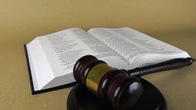 Open holy bible with a wooden gavel resting on its pages, representing the connection between divine law, moral principles, justice, and the legal system on a plain light brown background