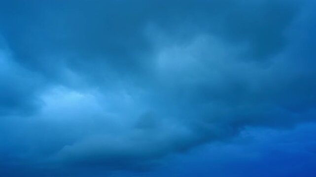 Dramatic storm clouds gathering in a deep blue sky with subtle light breaking through cinematic motion