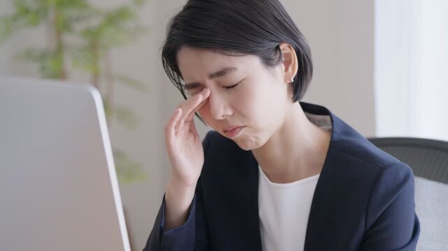 デスクトップパソコンで仕事をする眼精疲労のビジネスウーマン