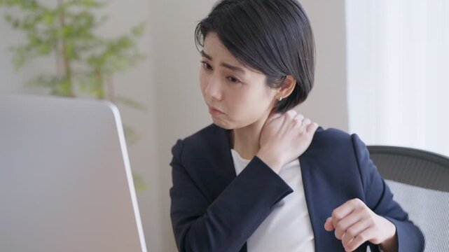 デスクトップパソコンで仕事をする肩こりのビジネスウーマン