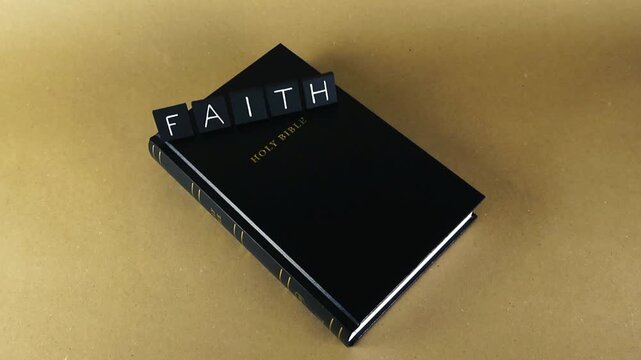 Closed Holy Bible with black letter tiles spelling the word faith on a light brown background, representing the conceptual basis of christian religion and spiritual belief in God