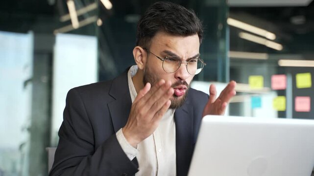 Angry businessman in a formal suit arguing talking on video call using laptop computer at workplace in business office. Excited dissatisfied executive quarrel with subordinate about problems. Close up