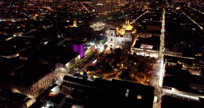 gorgeous night aerial drone view of the immaculate conception cathedral in cuenca ecuador surrounded by the glowing historic city skyline showcasing beautiful illuminated architecture under a dark sky