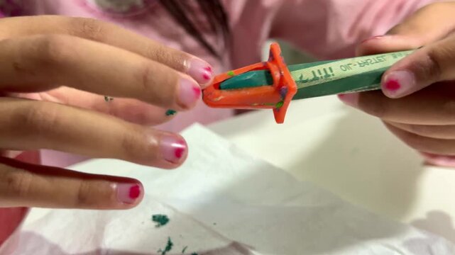 Kid hands sharpening crayon, colorful wax crayon, children's coloring and art supplies concept.
