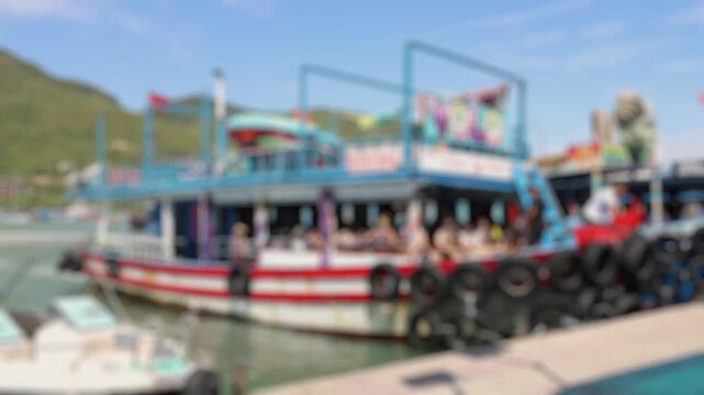 Bokeh view of Tourists boarding a colorful double-deck boat at the southern port in Nha Trang, Vietnam, with mountains in the background. Blurred background footage.