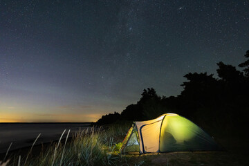 Illuminated camping tent on coastal beach under starry sky in Estonia © Dmitri