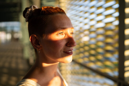 A woman smiles with sunlight creating shadows on her face indoors