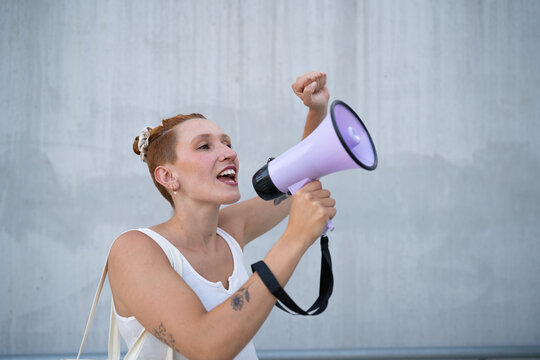 A white woman speaks passionately into a megaphone in an urban setting