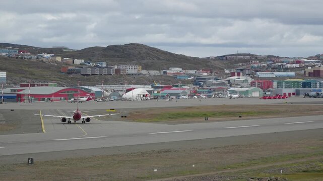 Wide perspective showing the Canadian North passenger jet taxiing on the foreground apron, with the line of bright red RAF Red Arrows fast jets parked in the background.
