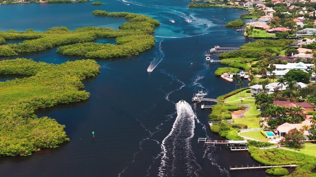 A leisure boat cruises along a dark tidal channel between mangrove islands and landscaped Osprey waterfront houses on a sunny day.