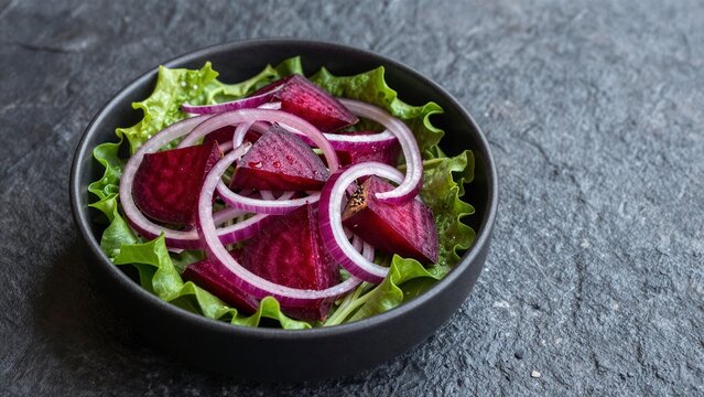 A vibrant beet and onion salad served on crisp lettuce leaves in a matte black bowl against a dark stone surface.
