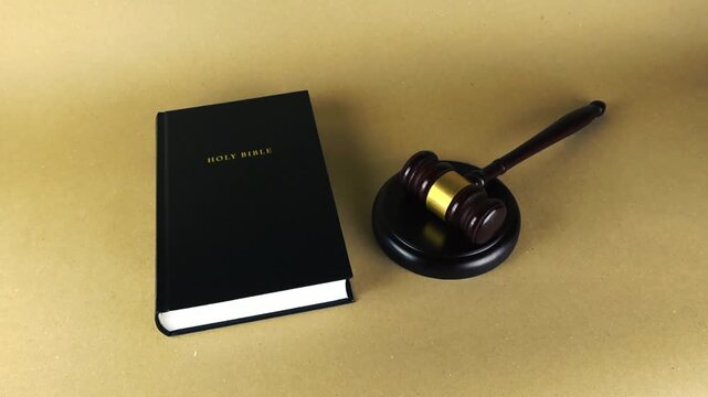 Holy Bible standing next to a judge's gavel on a neutral background, representing the conceptual relationship between divine law, religious principles, justice, and the legal system