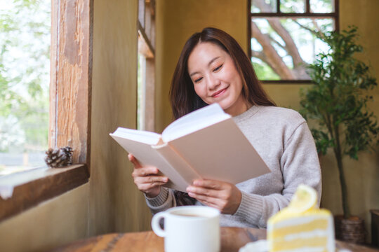 Portrait image of a woman reading a book with coffee cup and a lemon cake on the table