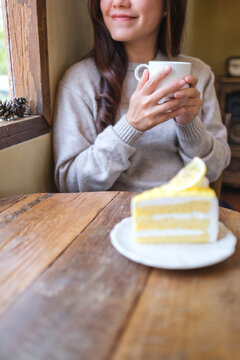 Vertical closeup image of a woman drinking coffee and eating a lemon cake in cafe