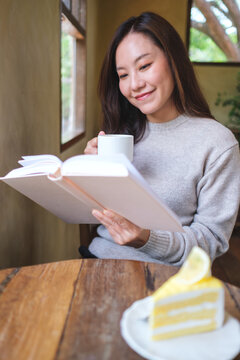 Vertical portrait image of a woman reading a book and drinking coffee in cafe