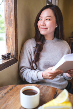 Vertical portrait image of a woman reading a book with coffee cup and a lemon cake on the table