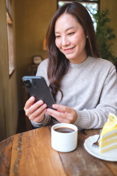 Vertical portrait of a woman holding and using mobile phone with coffee cup and cake on the table